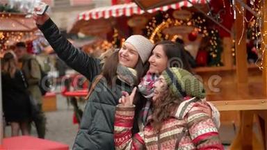 三个女朋友在圣诞市场上用智能手机自拍。 快乐的女人在圣诞快乐的户外活动